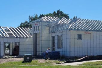House under construction with visible roof framing and white exterior panels.