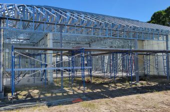 Steel frame structure being built under clear blue sky.