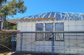House under construction with scaffolding and exposed roof framing.
