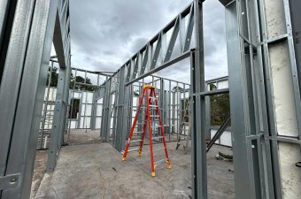 Steel frame structure with a red ladder inside under cloudy sky.