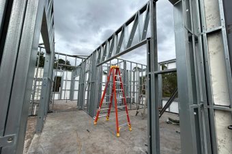 Steel frame structure with a red ladder inside under cloudy sky.