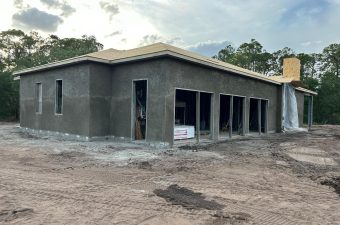 A newly constructed house with dark exterior walls under a cloudy sky.