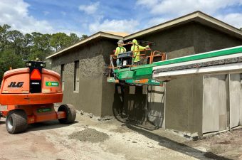 Construction workers applying stucco on a house exterior using a lift.