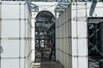 Construction site with scaffolding and protective coverings under a blue sky.