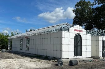 A unique white modular building with a black arched door under a blue sky.