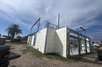 Metal-framed building under construction with palm trees