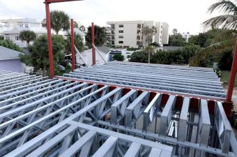 Steel framework of a building under construction with apartment buildings in the background.