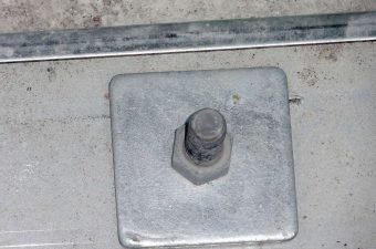Large bolt and square plate on a concrete surface with a metal ruler.