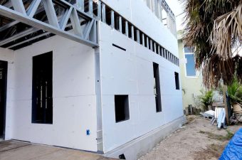 A newly painted white building exterior with some windows and a palm tree nearby.