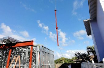A crane lifting a long red beam against a blue sky.