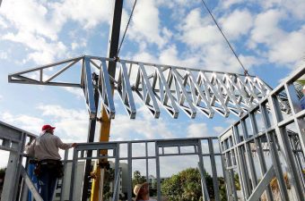 Workers installing a metal roof truss on a sunny day.