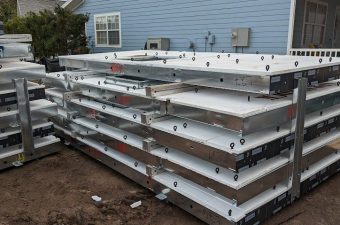 Stacked metal panels with insulation on the ground near a blue house.