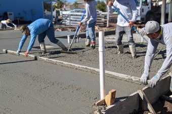 Workers leveling concrete near white PVC pipes