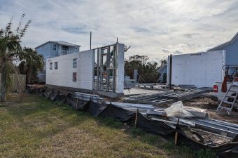 Partially constructed modular home sections on site under cloudy sky.