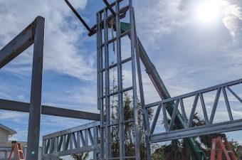 Workers assembling a steel structure under a sunny sky.