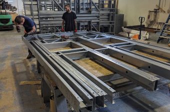 Workers assembling large metal frames in an industrial workshop.