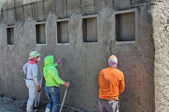 Three construction workers plastering a wall with small windows.