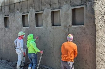 Three construction workers plastering a wall with small windows.