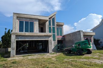 Modern two-story house under construction with large windows and a lift machine outside.