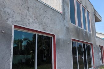 Unfinished concrete building with large glass windows and red frames.