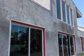 Unfinished concrete building with large glass windows and red frames.
