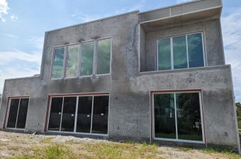 Unfinished two-story house with large windows under a clear sky.