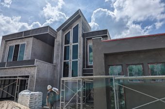 Modern two-story house under construction with large windows and glass railings.