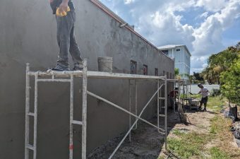 Workers applying cement plaster on an outdoor wall using scaffolding.