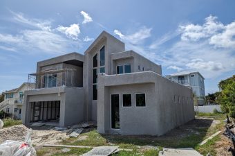 Modern house under construction with gray exterior walls and clear blue sky.