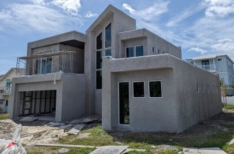 Modern two-story house under construction with gray exterior and large windows.