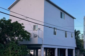 Three-story house elevated on stilts with clear blue sky.