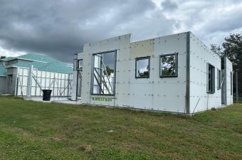 Partially constructed modern building with large windows under a cloudy sky.