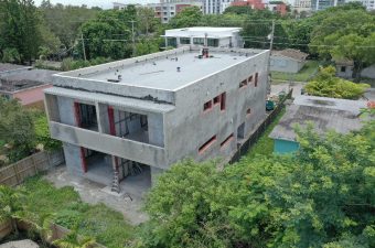 A large unfinished concrete building surrounded by greenery.