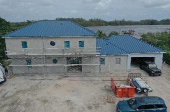 Two-story house under construction with blue roofing and scaffolding.