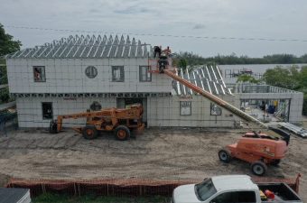 Workers install roofing panels on a large building under construction.