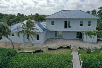 Modern two-story house with blue roof and a spacious backyard under cloudy sky.