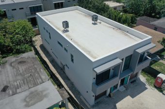 A modern white flat-roofed building with balconies and rooftop vents.